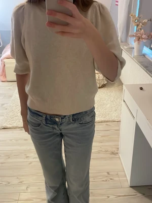 Ljusbeige stickad topp med puffiga armar - Ljusbeige stickad topp med rund hals och puffiga armar. Toppen har en avslappnad, normal passform och trekvartsärm som ger en chill vibe. Perfekt att matcha med jeans för en enkel och snygg look.