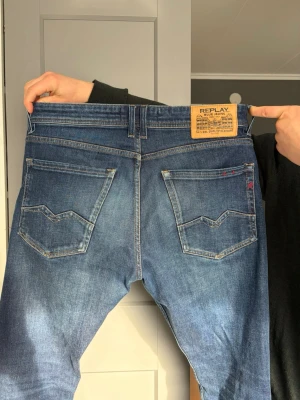 Blå Replay Rocco jeans comfort fit - Säljer ett par blå Replay Rocco jeans i comfort fit. Jeansen har klassisk femficksdesign, snygga slitningar och kontrastsömmar. Märkeslapp bak i midjan och Replay-detalj vid fickan. 