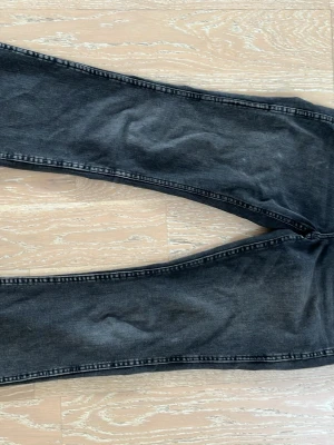 Svarta bootcut jeans i denim - Säljer ett par svarta bootcut jeans med tvättad finish och klassiska bakfickor. Jeansen har en lätt utsvängd passform nedtill och är sydda i mjukt denimtyg. Perfekta för dig som gillar en avslappnad och trendig look.