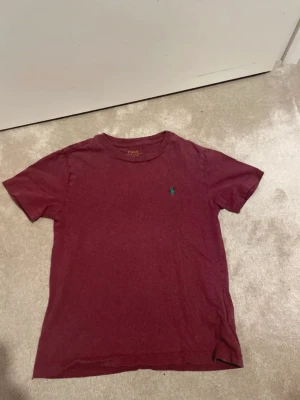 Vinröd t-shirt från Polo Ralph Lauren - Säljer en vinröd t-shirt från Polo Ralph Lauren med klassisk grön broderad logga på bröstet. T-shirten har rund halsringning och korta ärmar. Perfekt basic-plagg med snygg passform och mjukt bomullsmaterial.