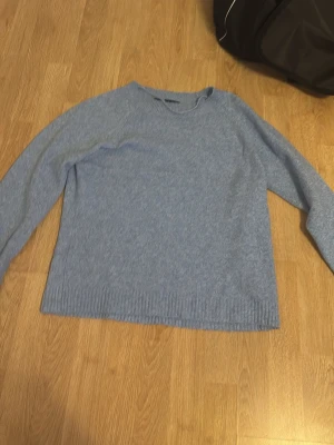 Ljusblå stickad tröja - Mysig ljusblå stickad tröja med rund halsringning och långa ärmar. Tröjan har ribbstickade muddar vid ärmslut och nederkant, vilket ger en klassisk och stilren look. Perfekt för lager-på-lager under kyliga dagar.