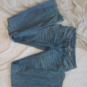 Blåa vida jeans med hög midja - Säljer ett par blåa jeans med breda ben och hög midja. Jeansen har klassisk femficksdesign, dubbla knappar i linningen och snygga slitningar framtill. Perfekta för en avslappnad och trendig look. Innerbensläng: 83 Midjemått:38. Litet håll som visas vid fickorna 