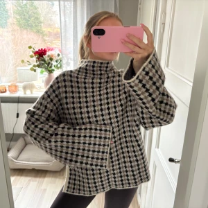 Svartvit stickad polotröja - Säljer en oversized stickad polotröja med svartvitt rutmönster. Tröjan har breda ärmar, hög krage och slitsar på sidorna. Perfekt för att hålla sig varm och snygg under kalla dagar. Materialet känns mjukt och tjockt.
