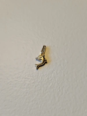 Halsbandshänge delfin i 18K guld - Snyggt halsbandshänge i form av en delfin, tillverkat i 18 karat guld. Hängsmycket har en stilren och lekfull design som passar perfekt till en tunn guldkedja. Märkt med 18K.
