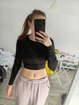 Svart croppad topp med snörning - Säljer en svart, croppad långärmad topp med snygg snörning och öppen rygg. Perfekt för dig som vill ha en trendig och edgy look. Materialet känns mjukt och stretchigt, vilket gör den bekväm att bära. Passar dig som gillar att sticka ut och vill ha något unikt i garderoben.