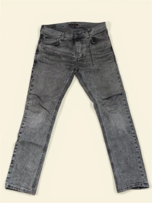 Grå raka jeans från nudie - Snygga grå jeans från nudi med rak passform och klassisk femficksdesign. Jeansen har en tvättad look och är tillverkade i slitstark denim. Perfekta för dig som gillar en avslappnad men stilren vibe. Har ett snitt vid knät som ger än snygg look 