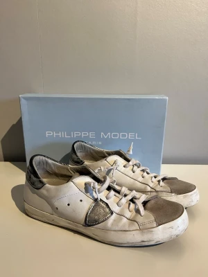 Philippe Model vita sneakers - Stilrena vita sneakers från Philippe Model med grå detaljer på tå och häl. Skorna har en låg silhuett, vita snören och är tillverkade i läder med mockadetaljer. Perfekta för en avslappnad och trendig look.