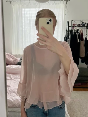 Ljusrosa volangblus från HM - Supersöt ljusrosa blus i transparent, lätt material med volangdetalj! Blusen har rund halsringning och vida, trekvartslånga ärmar. Perfekt att styla med jeans eller kjol nu i sommar! 