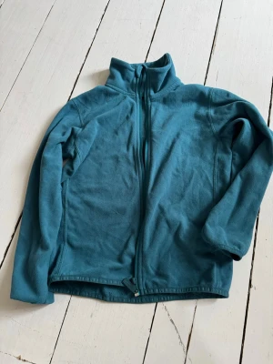 Turkos fleecejacka med dragkedja - Mysig turkos fleecejacka med hög krage och hel dragkedja framtill. Perfekt för lager-på-lager och chill dagar. Jackan har lång ärm och är tillverkad i mjuk fleece som håller dig varm.