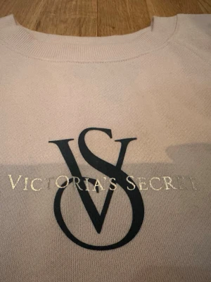Ljusrosa sweatshirt från Victoria's Secret - Ljusrosa sweatshirt från Victoria's Secret med stor VS-logga och text i silver på bröstet. Tröjan har rund halsringning, långa ärmar och ribbade muddar vid ärmslut och nederkant. Perfekt för en avslappnad och trendig look. Ord.pris 600 sek