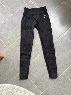 Svarta seamless leggings från Gymshark - Säljer ett par svarta seamless leggings från Gymshark med hög midja och diskret mönster längs benen. Stretchigt material som sitter tight och formar sig efter kroppen. Perfekta för träning eller chill dagar. Är 171 och storleken är S och är knappt använda