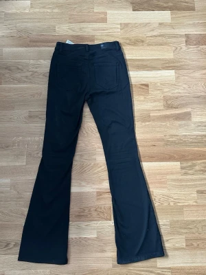 Svarta bootcut jeans från Vero Moda - Svarta bootcut jeans från Vero Moda med klassiska bakfickor och dragkedjegylf. Jeansen har en snygg utsvängd passform och är tillverkade i stretchigt denimtyg som sitter bekvämt. 