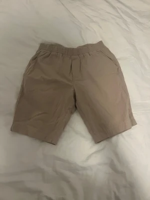 Beige shorts med resårmidja (linne) - Snygga beige shorts med elastisk midja och sidofickor. Perfekta för varma dagar och enkel att matcha med olika toppar. Tillverkade i ett lätt och bekvämt material som passar bra till sommaren.