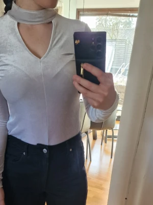 Ny ljuslila/grå sammets polotopp Gina Tricot med etikett - Supersnygg ljuslila polotopp från Gina Tricot i mjuk och glansig sammet. Toppen har lång ärm, lätt v-ringning och en smal passform som sitter snyggt på kroppen. Perfekt att styla med jeans eller kjol för en trendig look.