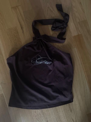 Brun halterneck topp med strassdetalj - Snygg brun halterneck topp med knyt i nacken och glittrande strassdetalj framtill. Stretchig. Aldrig kommit till användning Finns shorts till som man kan få med 