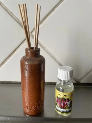 Doftspridare med keramikvas - Säljer en doftspridare med bruna doftpinnar i en rustik keramikvas och en flaska Honeysuckle doftolja från Colony. Perfekt för att fräscha upp rummet med en blommig doft. Vasen har en naturlig brun färg och enkel design.