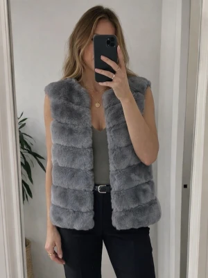 Grå pälsväst från by clara - Säljer en supermjuk och stilren grå pälsväst från by clara . Västen har en fluffig textur och är perfekt för att hålla värmen under kyliga dagar. Den är ärmlös och har en elegant design som passar till många olika outfits.
