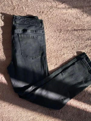 Svarta raka jeans från Denim - Snygga svarta jeans från Denim med rak passform och klassisk femficksdesign. Jeansen har knappgylf och bälteshällor, tillverkade i stretchigt bomullsmaterial för extra komfort. Perfekta till en avslappnad streetwear-look.