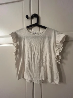 Vit topp med volangärmar - Söt vit topp med korta ärmar dekorerade med volanger. 