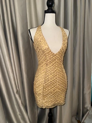Oh Polly glittrig guld klänning  - Snygg kort klänning i guld med glittriga paljetter och djup v-ringning. Klänningen är ärmlös och har ett figurnära snitt som framhäver siluetten.