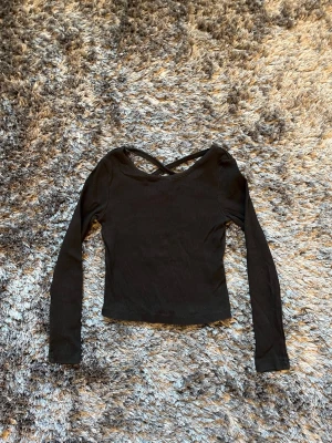 Svart ribbad topp med criss-cross - BARN/TONÅRINGAR: Svart långärmad topp med ribbad struktur och snygg criss-cross detalj vid ryggen från KAPPAHL. Modellen är croppad och har en figurnära passform. Perfekt att styla med jeans eller kjol. Använt några gånger. Strl 134/140.