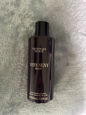 Victoria's Secret Very Sexy Night mist - En lyxig doftmist från Victoria's Secret, Very Sexy Night, i en elegant mörklila plastflaska med guldfärgad text. Flaskan rymmer 250 ml och har en stilren, cylindrisk form. Perfekt för dig som vill ha en sensuell och exklusiv doft.❤️‍🔥