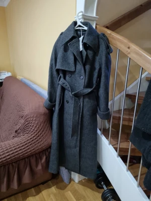 Kappa Other & Stories - Stilren mörkgrå trenchcoat i ullmix med klassisk dubbelknäppning, bred krage och axelklaffar. Knyt bältet i midjan för en snygg siluett. Långa ärmar med uppvikta muddar och slits bak. Perfekt för dig som vill ha en tidlös och trendig look. Nypris 5490kr