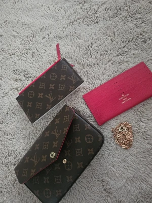  monogram väska - Säljer en snygg handväska med plånbok i klassiskt brunt monogrammönster med rosa detaljer. Plånboken har kuvertformad design, guldknapp och insida i rosa. Tillverkad i tåligt canvasmaterial och har flera fack för kort och sedlar.
