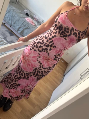 Leopardmönstrad långklänning med rosa blommor - Säljer en långklänning med leopardmönster och stora rosa blommor. Klänningen har smala axelband och figurnära passform. Perfekt för dig som vill sticka ut med ett unikt mönster och coola detaljer.