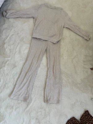 Beige ribbat loungewear-set - Mysigt loungewear-set i beige med ribbad struktur. Setet består av långärmad tröja med rund hals och matchande byxor med utsvängda ben. Tröjan har även en huva för extra komfort. Perfekt för chill dagar hemma.