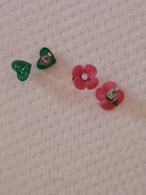 Örhängen  - Handgjorda örhängen med blomma  Söta örhängen i form av rosa blommor. Ett lekfullt och romantiskt smycke som passar både till vardag och fest.  Handgjorda örhängen med hjärta  Glittrande gröna hjärtan som ger en färgstark och personlig detalj till din stil. Lätta och charmiga att bära. Båda 100 kr ,en 55 kr