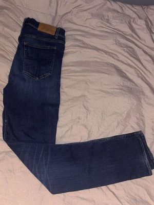 Mörkblå raka jeans av tiger of sweden - Säljer ett par mörkblå jeans med klassisk femficksdesign och raka ben. Jeansen har en snygg läderpatch bak i midjan och kontrastsömmar. Perfekta till en avslappnad stil och tillverkade i mjukt denimtyg. Väldigt snygga passar alla väldigt bra och modellen heter Leon