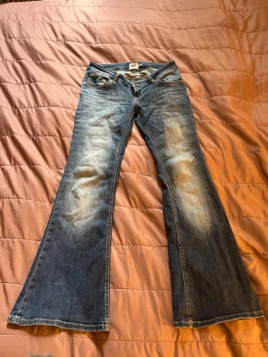 Blå bootcut jeans från lager 157 - Säljer ett par blå bootcut jeans från lager 157 i storlek M med kort längd. Jeansen har klassisk femficksdesign, dragkedja och knapp framtill. Materialet är bomull och passformen är loose med breda ben. Perfekt för dig som gillar retrostil och bekväma jeans.