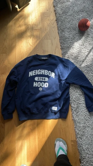  NEIGHBORHOOD sweater - Mörkblå sweatshirt från NEIGHBORHOOD med vit tryckt text 'NEIGHBORHOOD 3204 HOOD' på bröstet. Klassisk rund halsringning och ribbade muddar vid ärmslut och nederkant. Perfekt för en avslappnad streetwear-look. Mycket hög kvalité eftersom den är från Japan. Knappt använd, passar som en boxy medium eftersom den följer japanska storlekar. Nypris över 2000 spänn men ja kan låta den vandra vidare för 1000, pris går såklart att diskuteras 