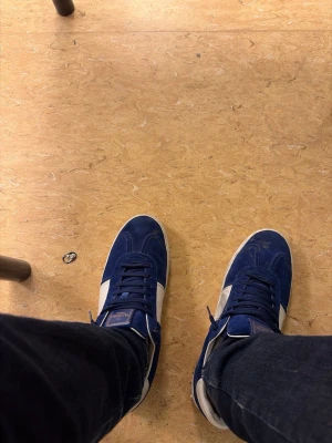  valentino Opens - Säljer ett par blåa sneakers från valentino med vita detaljer på sidorna och mörkblå snörning. Skorna har en klassisk låg profil och är tillverkade i mocka med gummisula. Perfekta för dig som gillar retrostil och vill sticka ut med