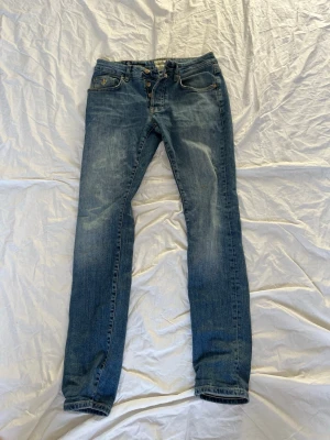 Blå Morris Jeans slim fit 29/32 - Snygga blå jeans från Steve Jeans i modellen slim fit. Jeansen har klassisk femficksdesign, normalhög midja och lätt slitna detaljer framtill. Perfekta för dig som gillar en smalare passform och tidlös denimstil.