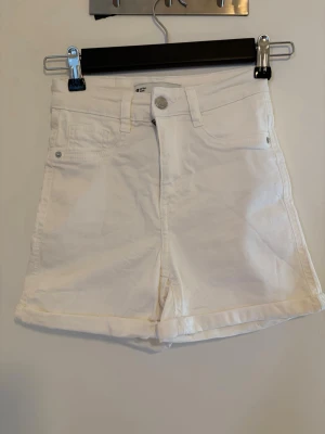 Vita jeansshorts Molly XS - Snygga vita jeansshorts från Gina Tricot, modell Molly. Klassisk femficksdesign, knapp och dragkedja framtill samt upprullade benslut. Perfekta till sommaren och lätta att matcha med allt.