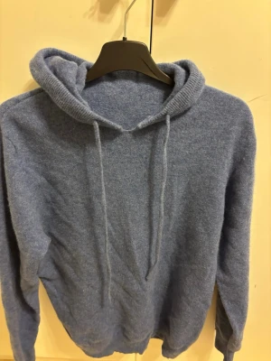 Blå mjuk hoodie - En stilren blå hoodie i mjukt material med huva. Klassisk passform och ribbade muddar vid ärmslut och nederkant. Perfekt för chill dagar eller när du vill ha något bekvämt och enkelt.