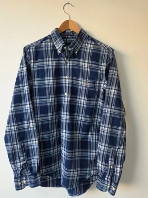 Blårutig skjorta från GANT stl M - Säljer en klassisk blårutig skjorta från GANT med vit och grå detalj. Skjortan har långärmad design, knappar framtill och bröstficka med broderad logotyp. Perfekt för dig som gillar en tidlös och stilren look.