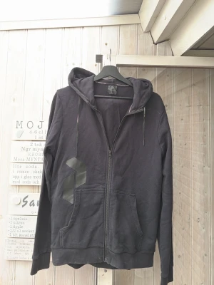 peak performance zip tröja  - Svart hoodie med dragkedja från Black Diamond. Hoodien har två stora fickor framtill, justerbar huva med snören och en matt svart logga på vänster sida. Tillverkad i mjukt bomullsmaterial som är skönt att bära. Tveka inte med att höra av dig