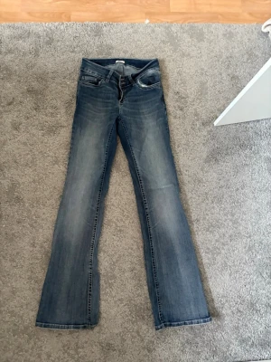 Blå bootcut jeans från Nelly - Säljer ett par blå bootcut jeans från Nelly med klassisk stil med dubbla knappar. Jeansen har en snygg tvättad look och bootcut. Nypris 699.