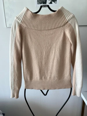 Beige stickad tröja Linn Ahlborg x NA-KD - Beige stickad tröja med bred ribbad krage och kontrasterande ljusa ärmar. Tröjan har långa ärmar och ribbade muddar vid ärmslut och nederkant. Perfekt för lager-på-lager och en stilren look.