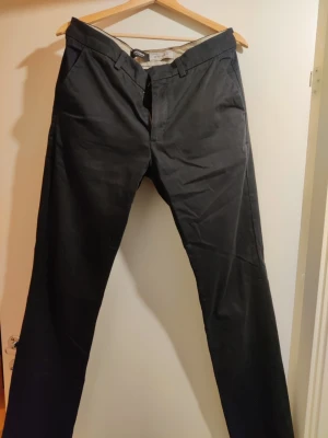 Svarta chinos från Dockers Extra Slim fit W33 L34 - Snygga svarta chinos från Dockers i extra slim fit-modell. Byxorna har klassisk design med snedställda fickor fram och bälteshällor. Perfekta för dig som gillar en smalare siluett och stilren look. Storlek W33 L34