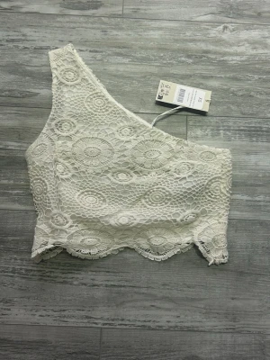 Vit spetsblus oneshoulder - Säljer en vit oneshoulder-blus från NA-KD storlek XS. Blusen är gjord i vacker spets med blommigt mönster och har en asymmetrisk skärning. Perfekt för dig som vill ha en unik och trendig topp med fina spetsdetaljer.