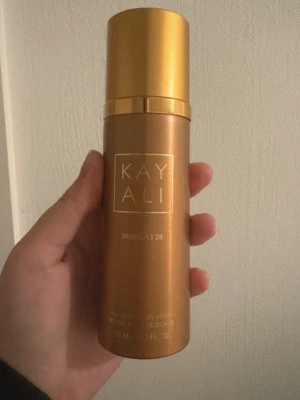 Kayali Vanilla | 28 Body Spray - Kayali Vanilla | 28 är en lyxig body spray i en snygg, guldig flaska med metallisk finish. Doften har tydliga vaniljtoner och flaskan har en elegant, rundad form med guldfärgat lock. Perfekt för dig som älskar söta och varma dofter.