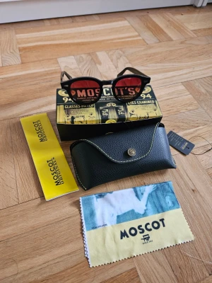 Svarta Moscot solglasögon med röda glas - Snygga solglasögon från Moscot med rund svart båge och röda tonade glas. Klassisk och trendig design som sticker ut. Kommer med originalfodral, putsduk och box. Perfekt accessoar för dig som vill ha något unikt och stilrent.
