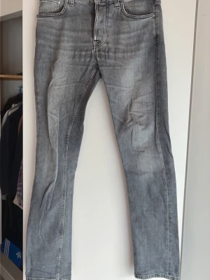 Grå jeans från Nudie Jeans - Säljer ett par grå tvättade jeans från Nudie Jeans med klassisk femficksmodell och raka ben. Jeansen har snygga slitningar och kontrastsömmar på bakfickorna. Perfekta för en avslappnad och trendig stil.