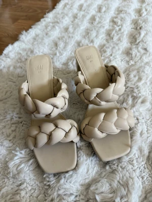 Beige flätade sandaler H&M - Snygga beige sandaler från H&M med breda, flätade remmar och fyrkantig tå. Sandalerna har en chunky blockklack och är gjorda i mjukt syntetmaterial som ger en modern vibe. Perfekta för dig som gillar trendiga detaljer och stilren design.