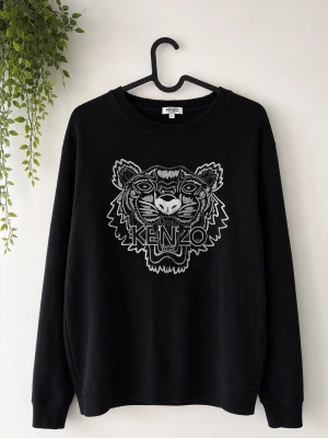 Svart sweatshirt  Kenzo - Cool svart sweatshirt från Kenzo med ett stort, broderat tigerhuvud och logga på bröstet. Tröjan har rund halsringning och ribbade muddar vid ärmslut och nederkant. Perfekt för dig som gillar streetwear och vill sticka ut med en ikonisk design.