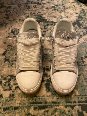 Vita och grå sneakers från Numeris - Snygga sneakers från Numeris i vitt och ljusgrått med ett unikt kamouflagemönster. Skorna har tjocka vita snören, räfflad sula och tåparti i strukturmaterial. Perfekta för dig som vill sticka ut med en modern och fräsch look.